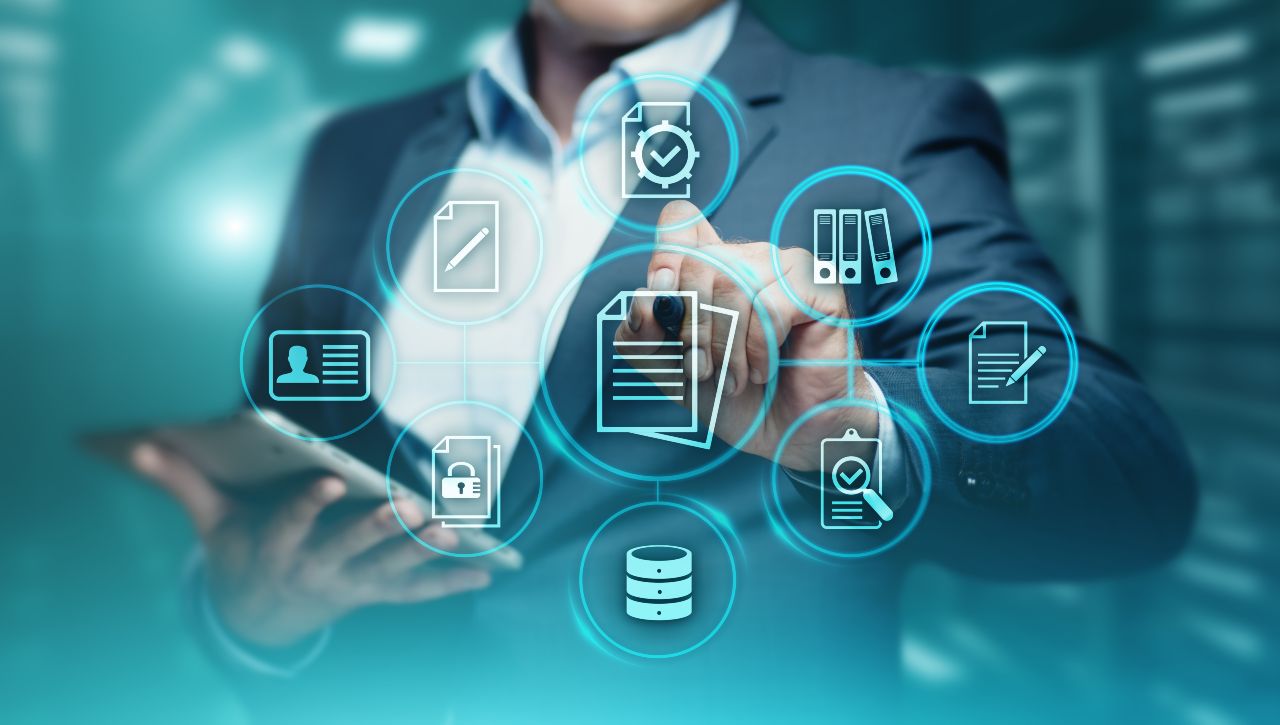 Oseba v poslovni obleki uporablja tablico in virtualni vmesnik z ikonami za dokumente in podatke.